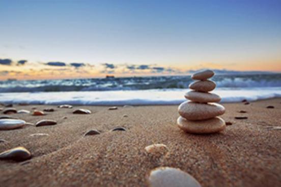 Ground level view of the beach, with tide coming in.  5 rocks, on on top of another is on the right side. 