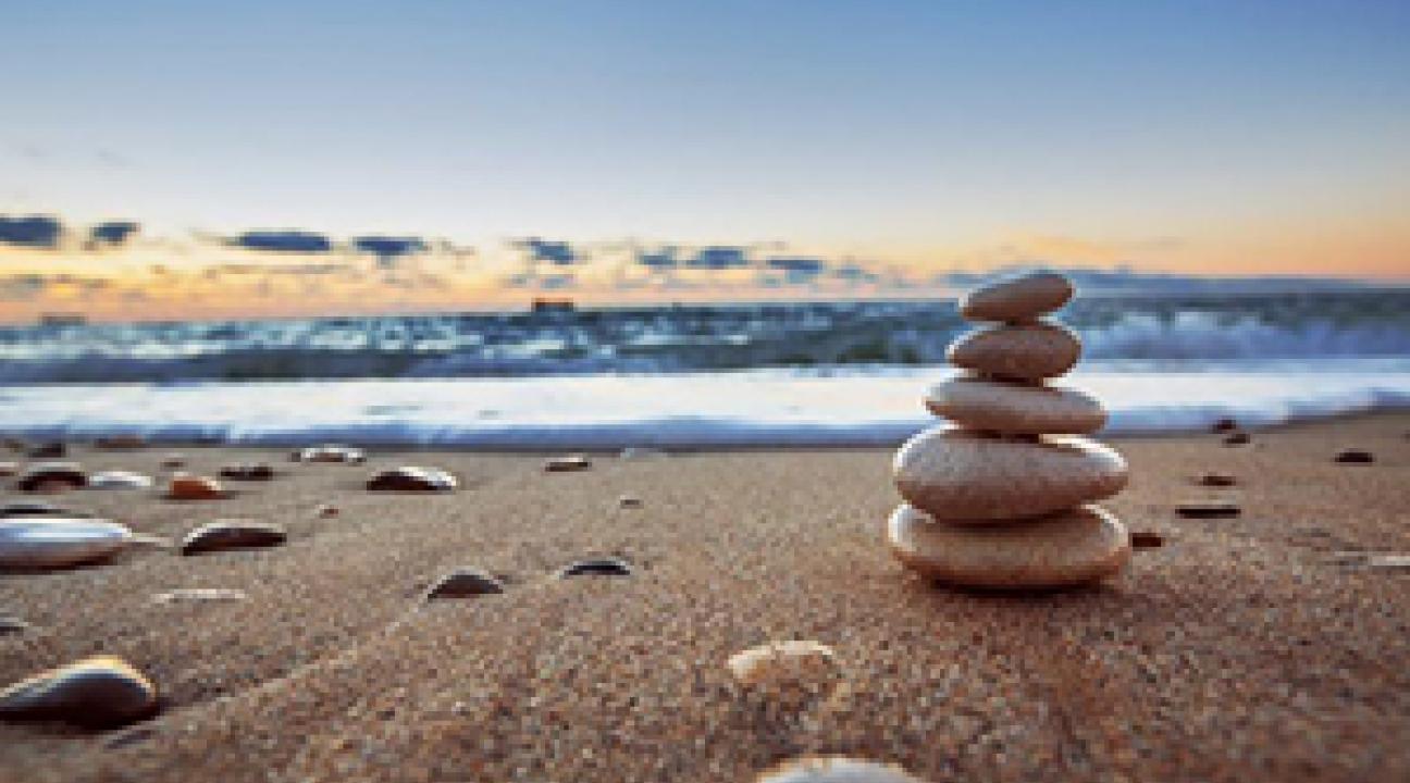 Ground level view of the beach, with tide coming in.  5 rocks, on on top of another is on the right side. 